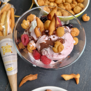 A mixed bowl of ice cream, chocolate and raspberries with toppings of Chin Chin with a custom packaged Chin Chin next to the bowl.