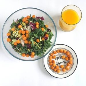 A bowl of salad topped with Chin Chin, A plate of Chin Chin and a glass of juice.