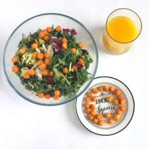 A bowl of salad topped with chin chin kept aside a bowl of chin chin. there is also a glass of orange juice